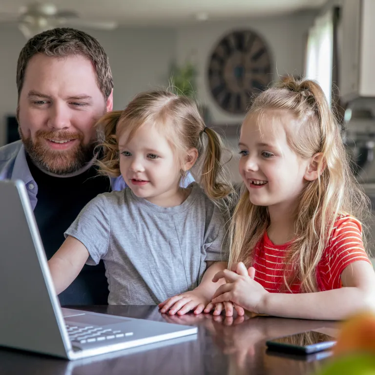 padre con dos hijas mirando la pantalla de una computadora