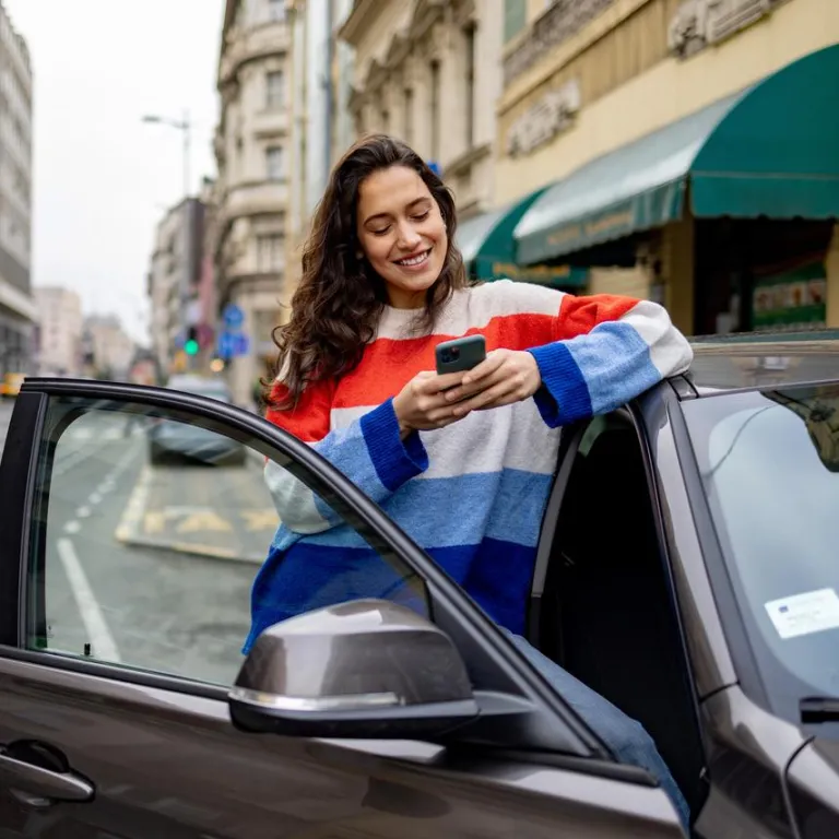 mujer al lado de un auto mirando el celular