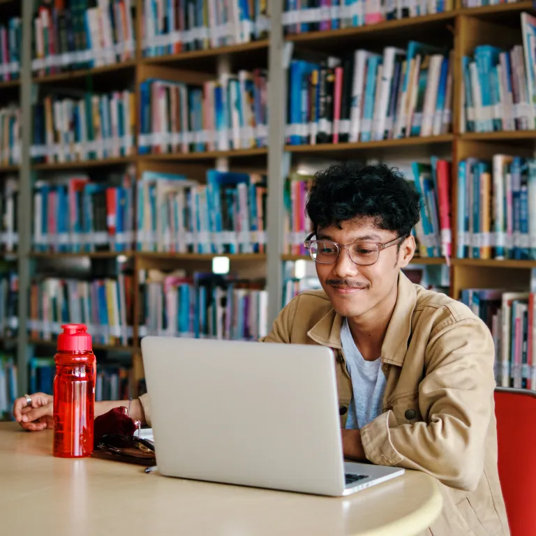 hombre joven estudiando con la computadora en una bibloteca
